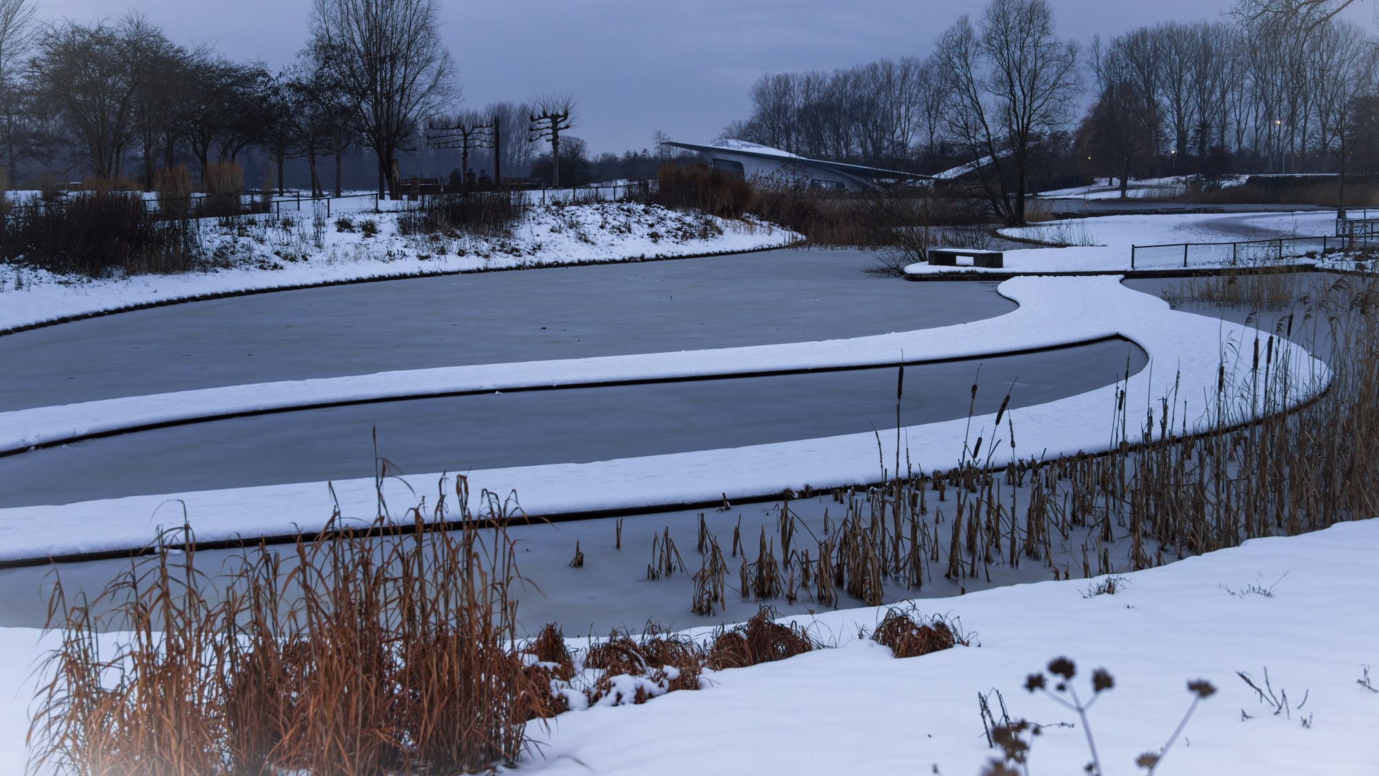 Frozen pond with an S-curve of snow on the ice in the blue hour, Netherlands