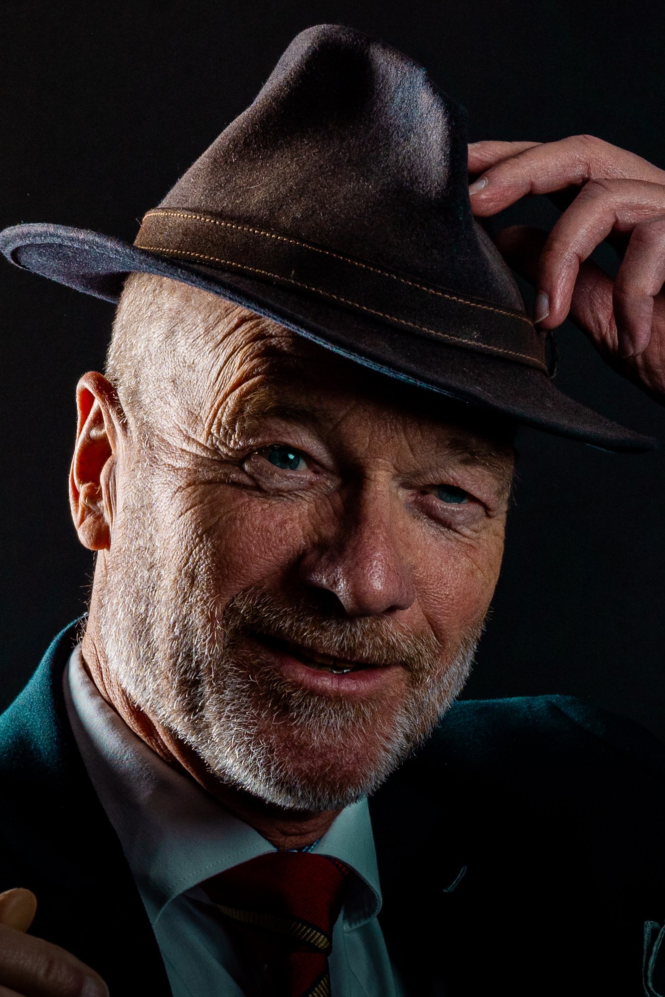 Man tipping his felt hat, warm side light on a characterful face, studio portrait on black